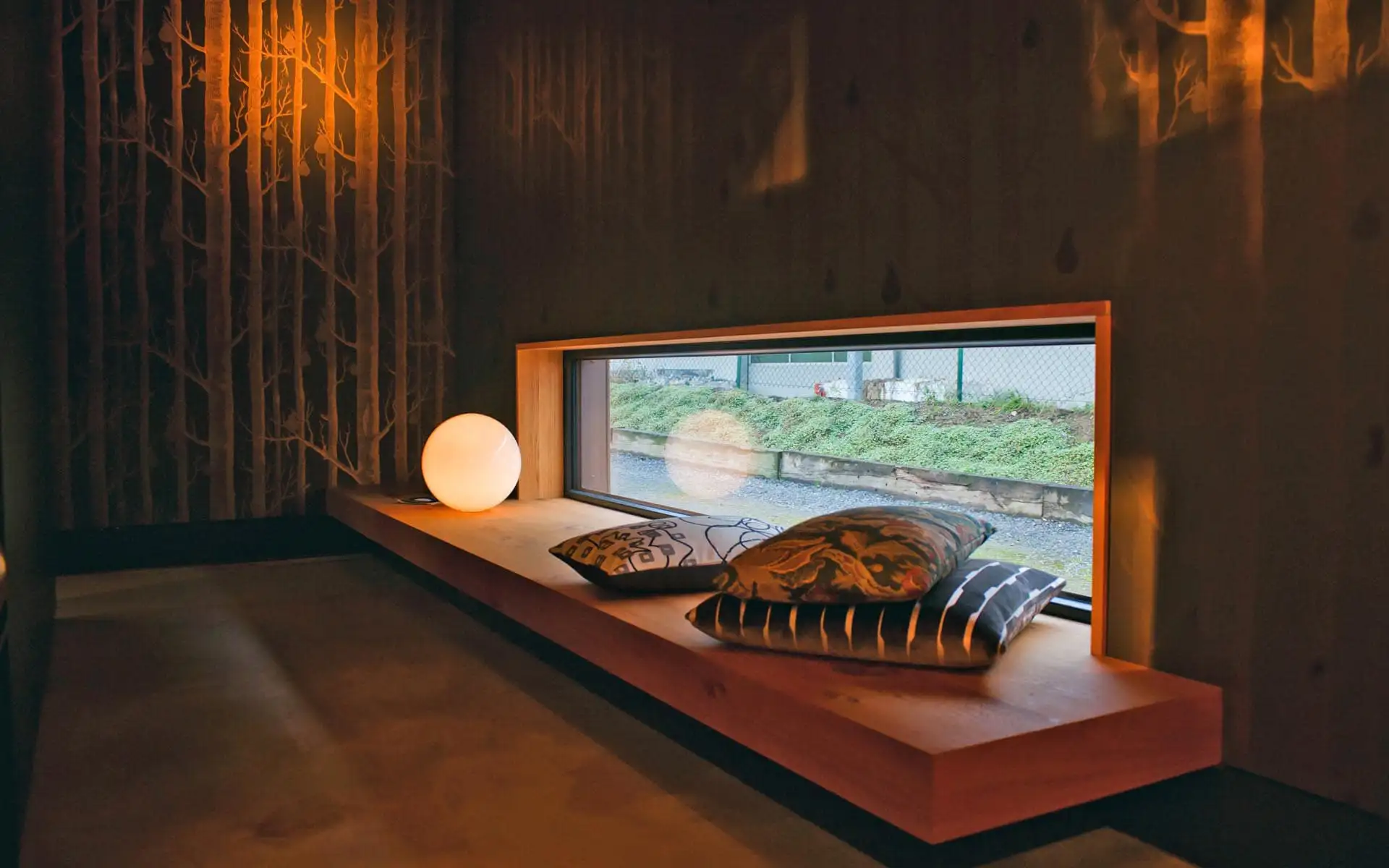 Fensternische mit breiter Holzbank, Kissen und indirekter Beleuchtung in einem ruhigen Innenraum.