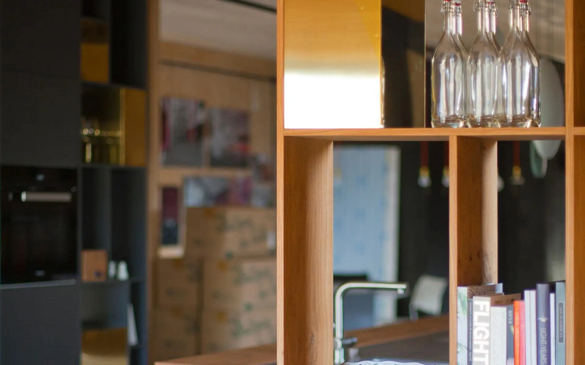 Detail einer Regalstruktur aus Holz mit integrierter Leuchte, Flaschen und Büchern.