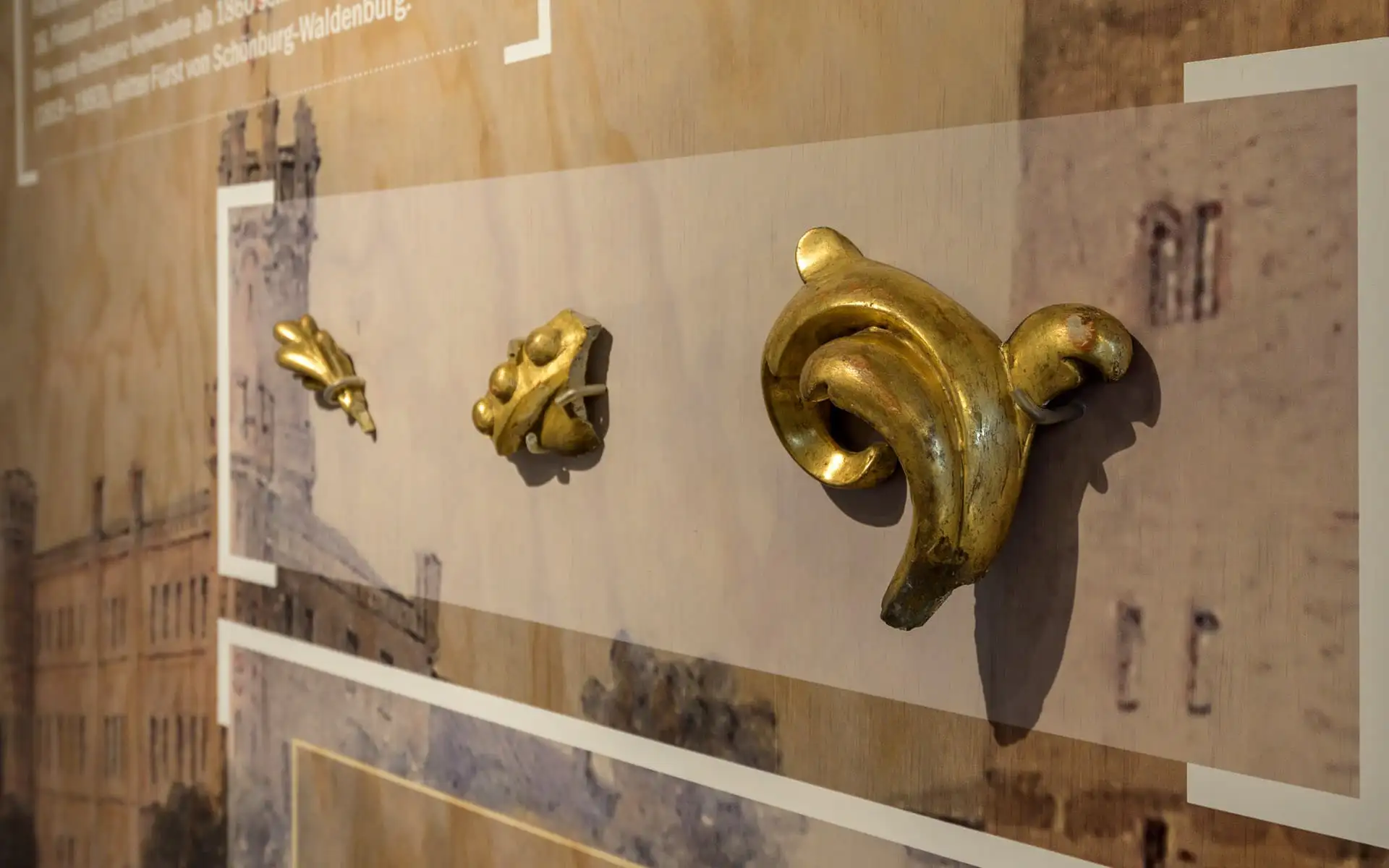 Detail einer Ausstellungstafel mit vergoldeten Architekturfragmenten vor historischen Abbildungen