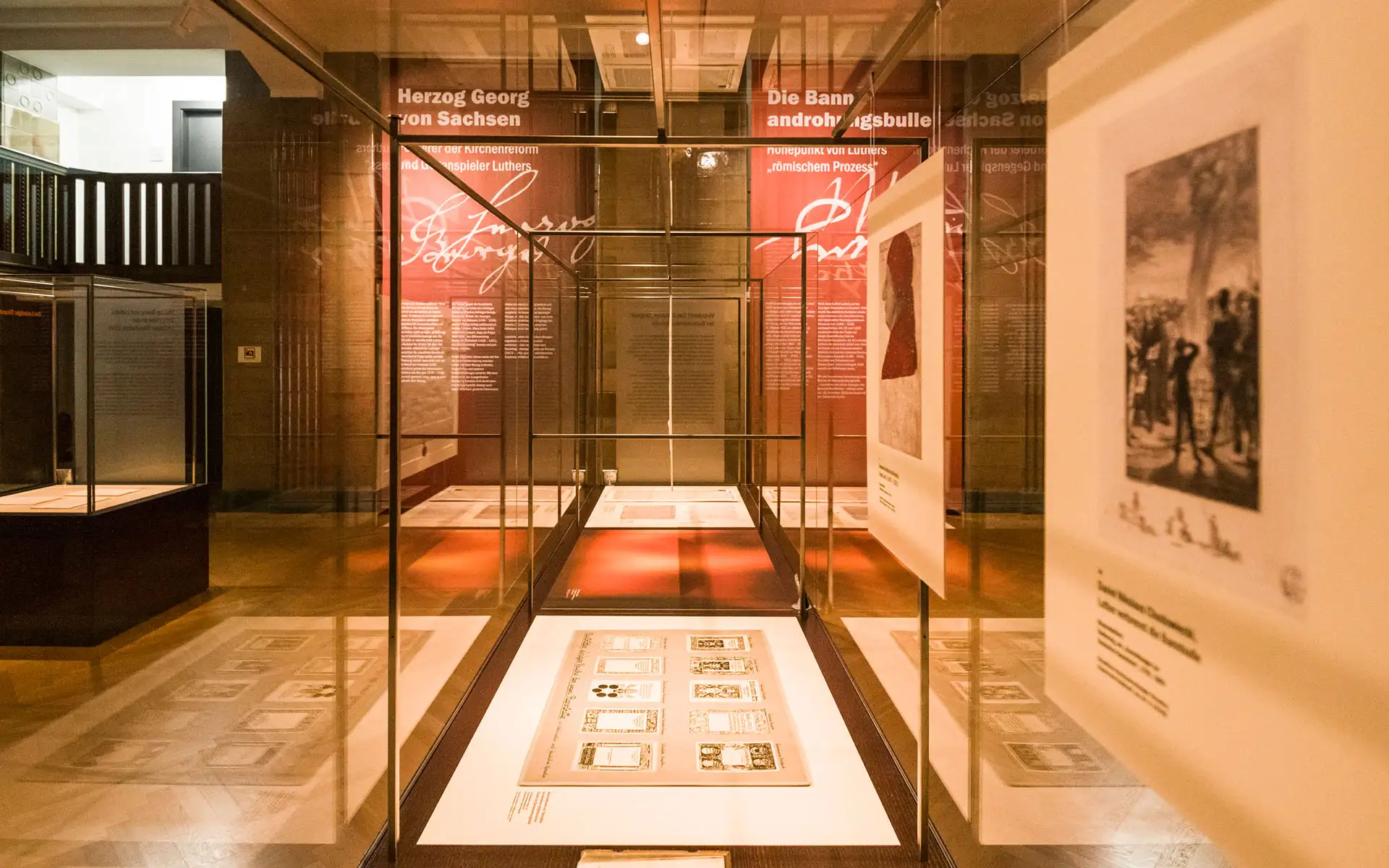 Blick durch gläserne Ausstellungsvitrinen mit großformatigen Blättern; im Hintergrund Wandtexte zur Kirchenreform und zur Bannandrohung