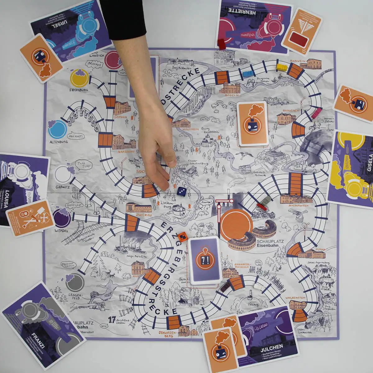 Brettspiel von oben mit Spielplan, Karten und einer Hand über dem Spielfeld