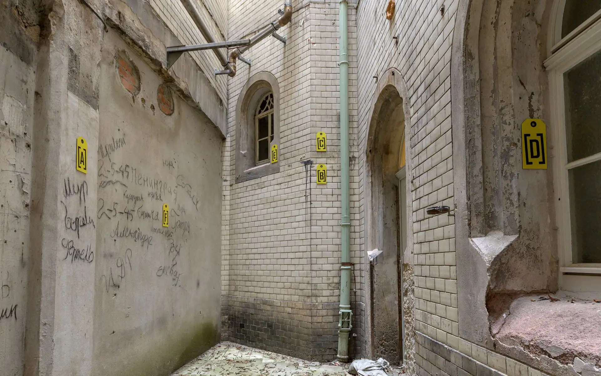 Schmaler Innenhof mit alten Fliesenwänden, Fallrohr und gelben Markierungen an den Wänden