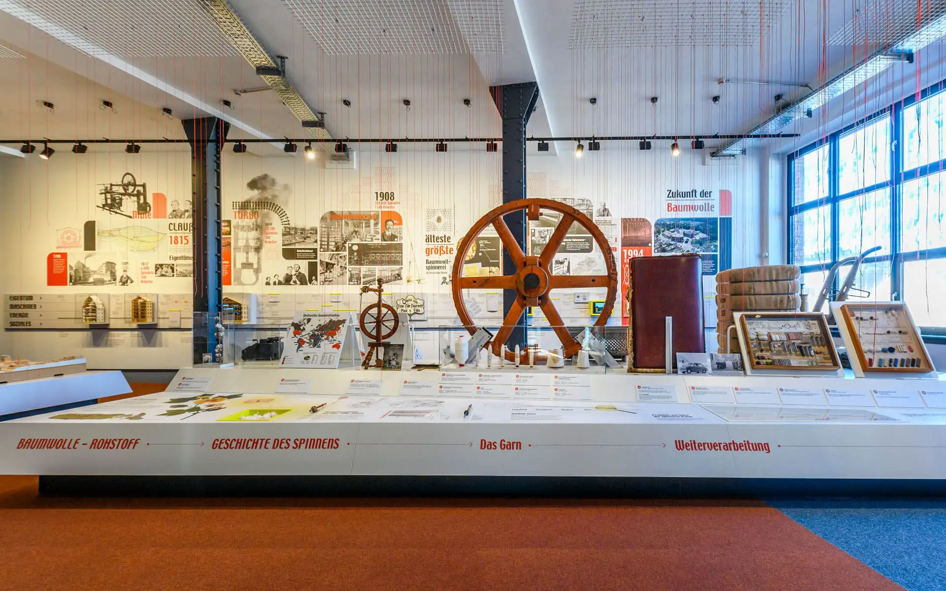 Großer Ausstellungsraum mit zentraler Präsentationsfläche und historischem Antriebsrad