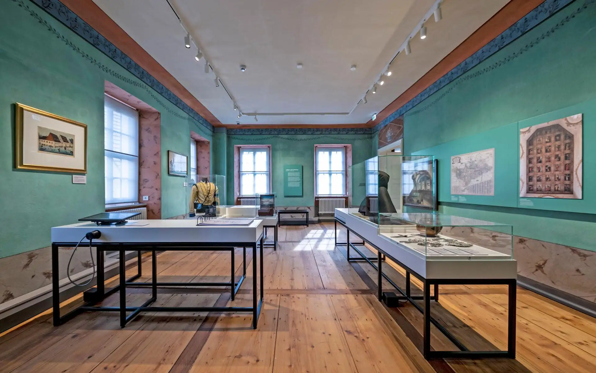 Historischer Ausstellungsraum mit türkisen Wänden, Vitrinen und Grafiken