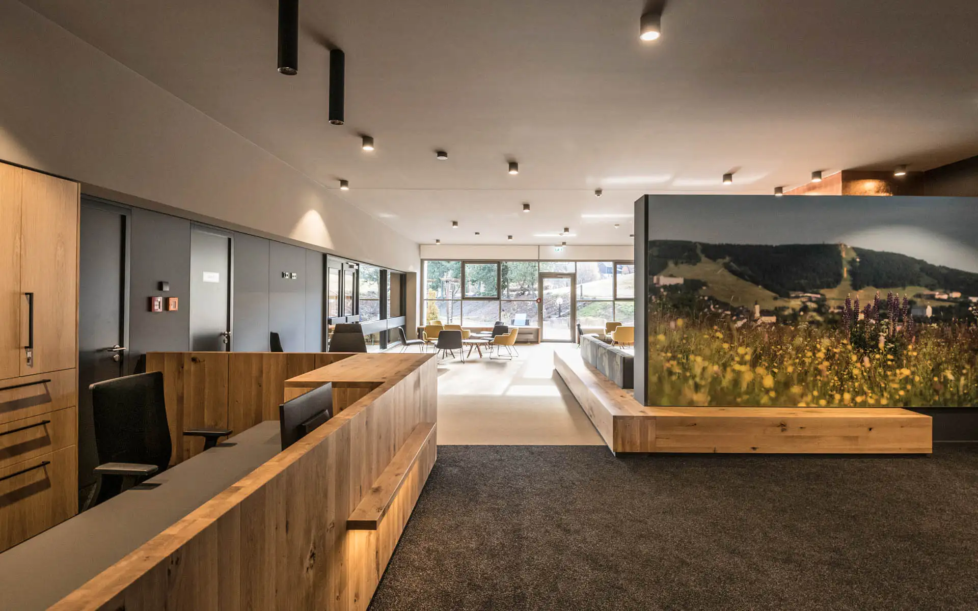 Große Lobby mit Holzempfang, Sitzbereich und weitem Blick durch bodentiefe Fenster ins Freie.