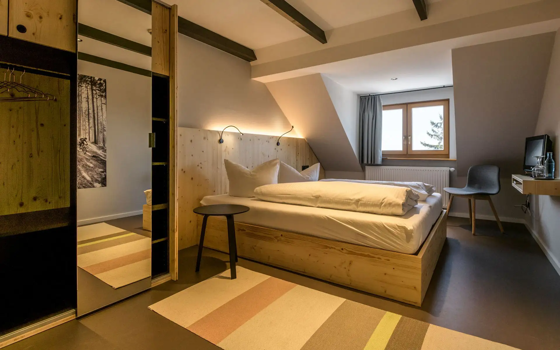 Doppelzimmer mit Holzbett, indirekter Beleuchtung, Teppichläufer und kleiner Arbeitsplatz-Nische mit Fernseher.