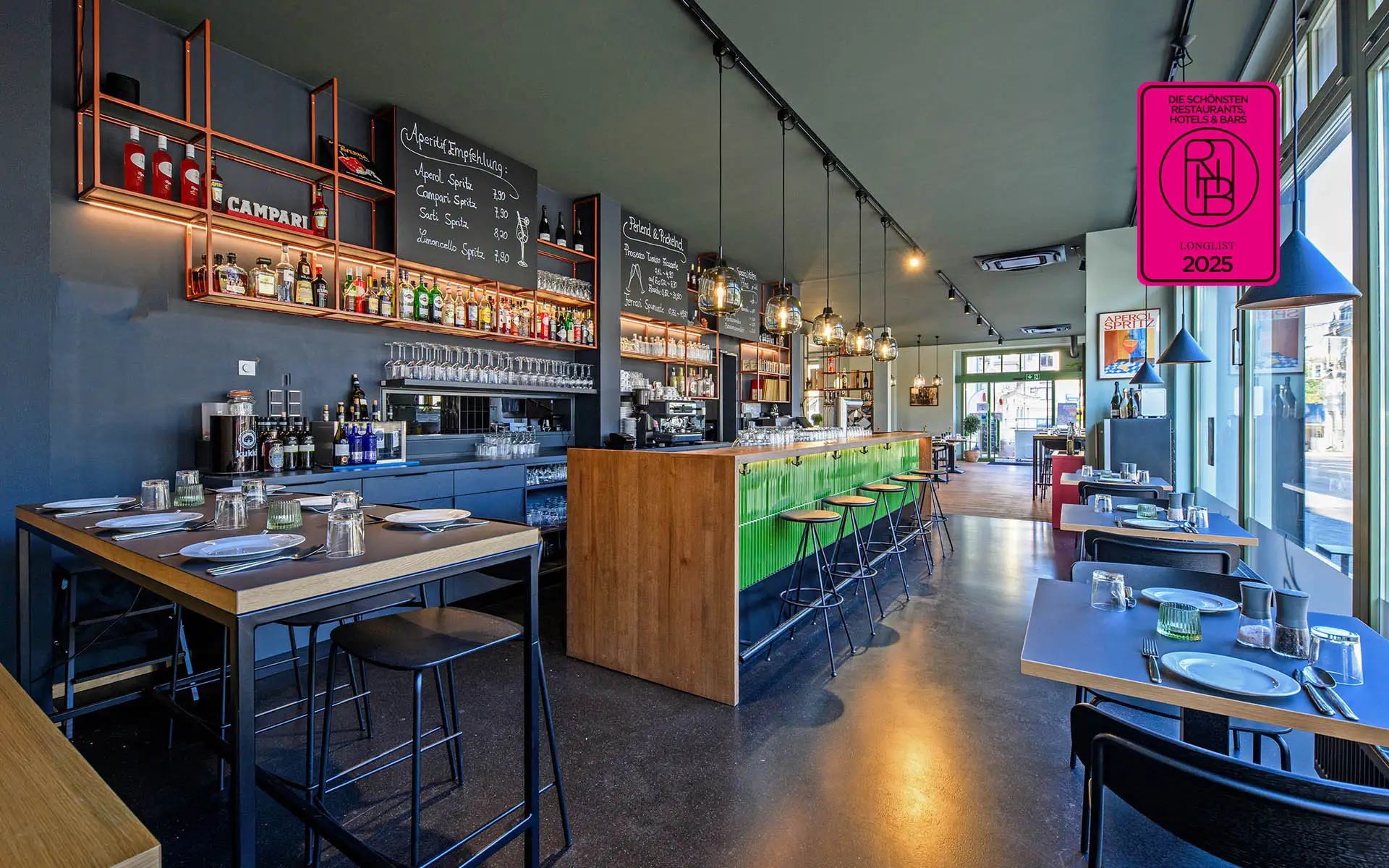 Innenansicht des Restaurants mit grüner Bartheke, schwarzen Barhockern, gedeckten Tischen und großen Fenstern zur Straße.