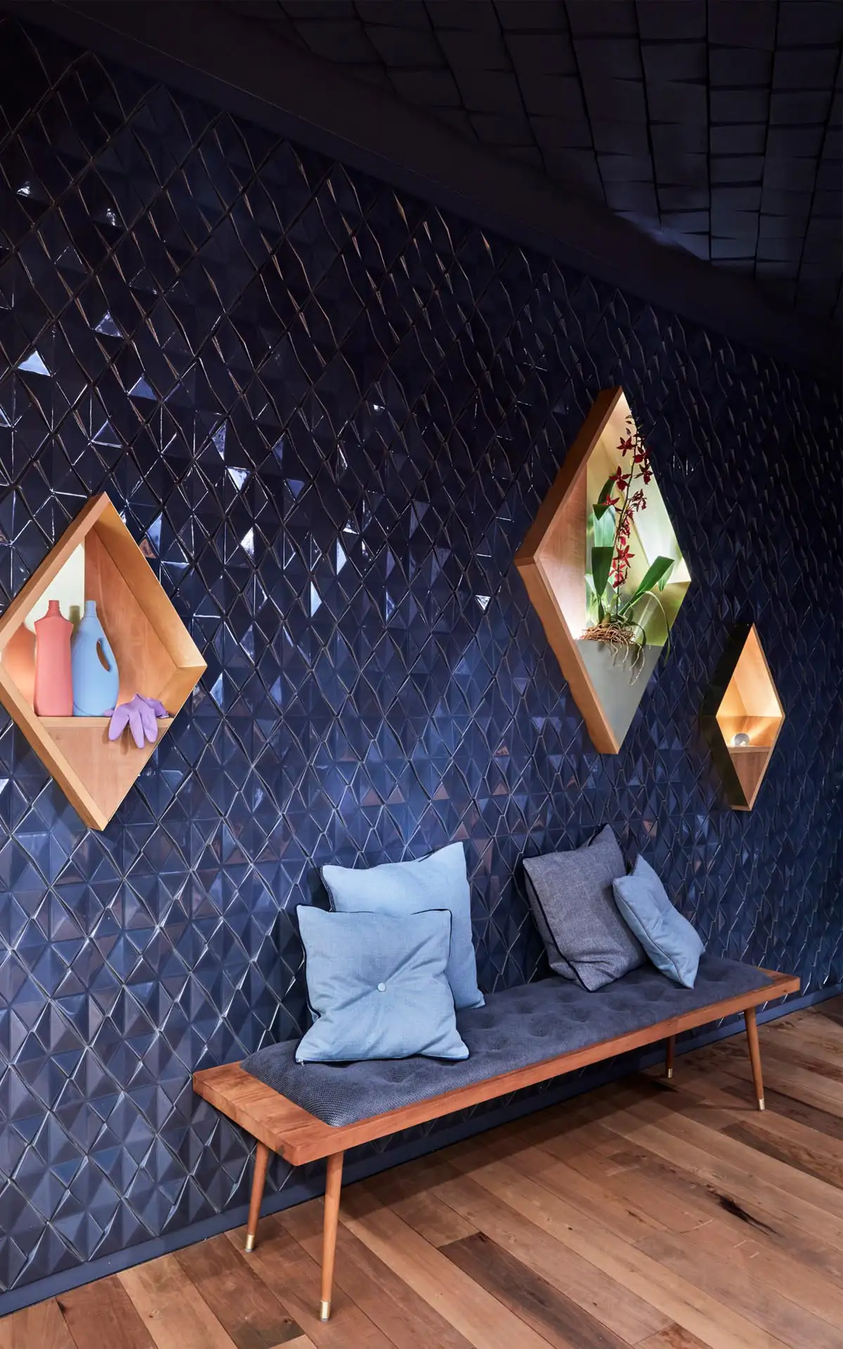 Sitzecke mit Bank und Stuhl vor glänzender blauer Strukturwand und beleuchteten Wandnischen.