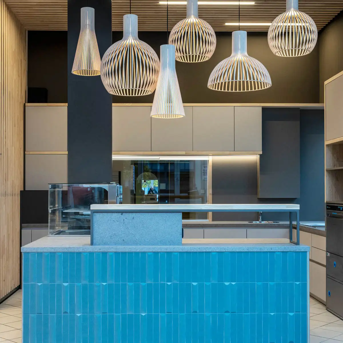 Frontansicht der Cafétheke mit vertikalen Keramikfliesen, integrierter Technik und ruhiger, moderner Farbgestaltung.