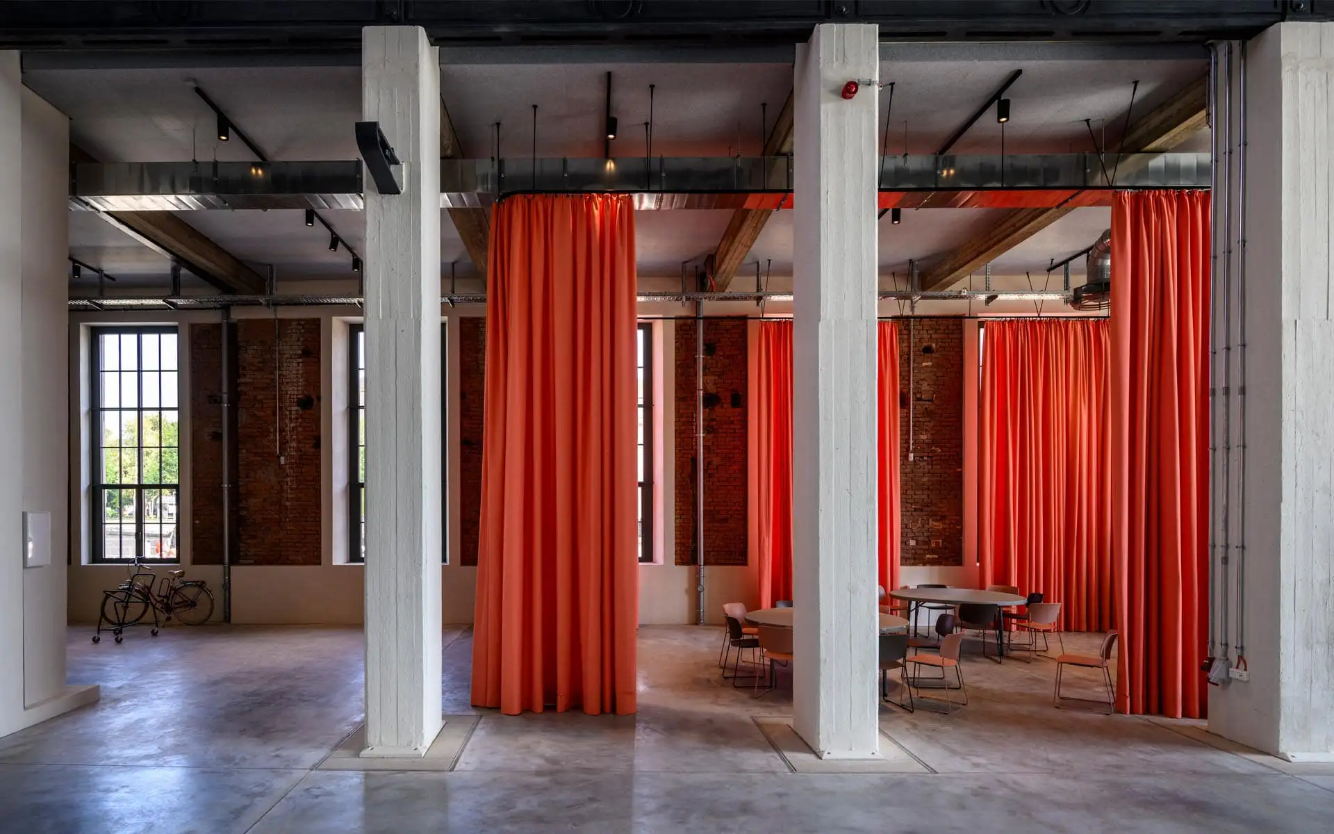 Großer Raum mit hohen weißen Stützen und raumteilenden orangefarbenen Vorhängen.