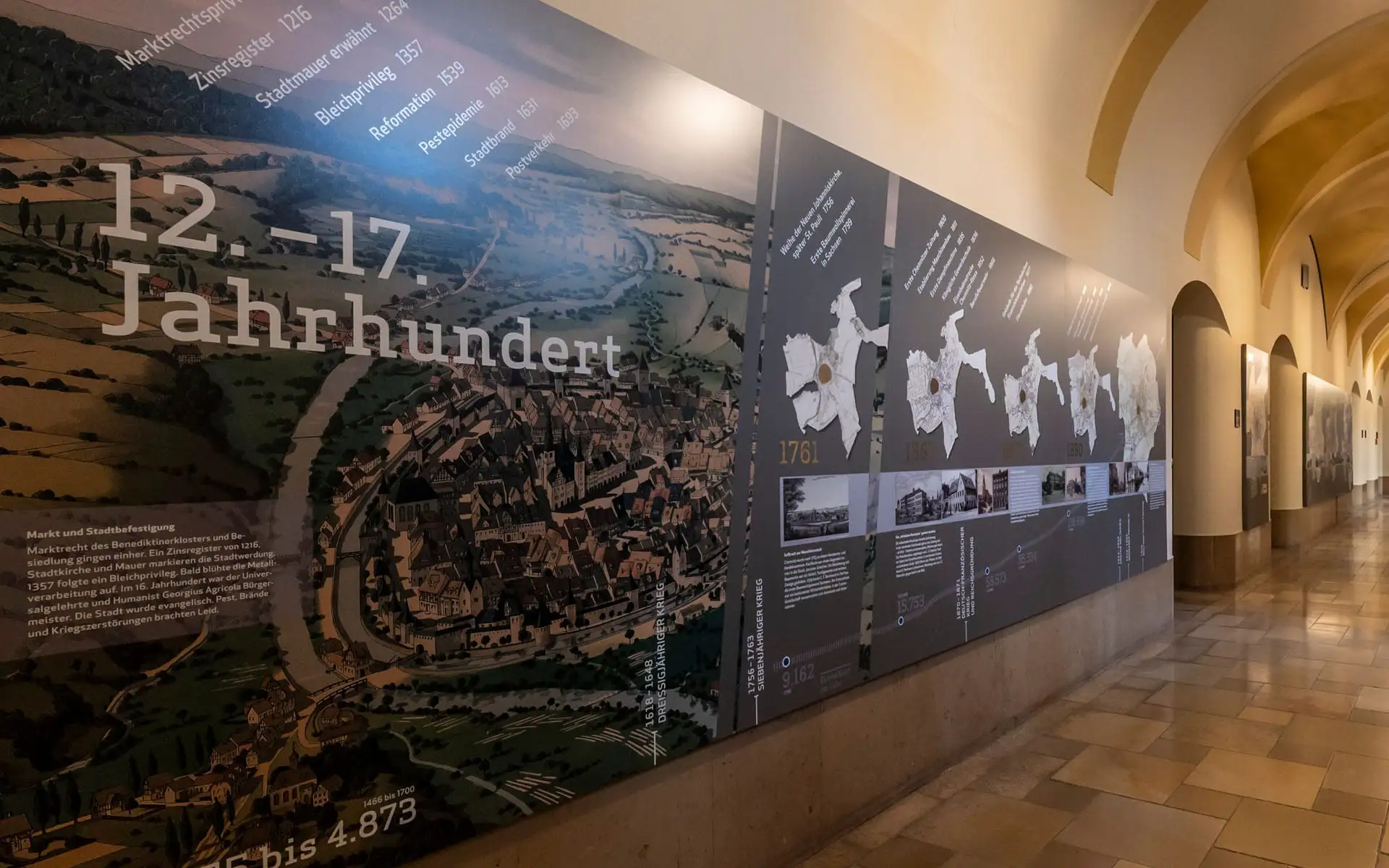 Wandinstallation mit ausgeschnittenen Stadtplänen; gold markierte Altstadt, Blick entlang des Flurs