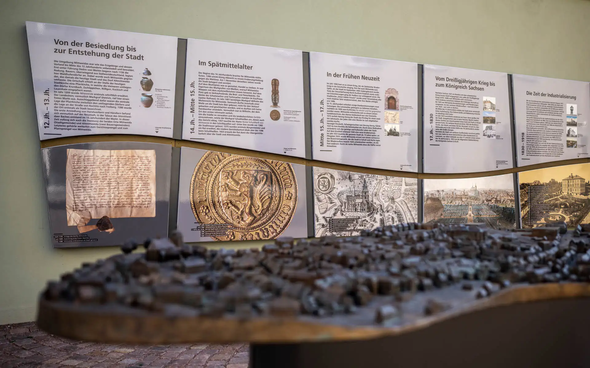 Nahaufnahme des Bronze-Stadtmodells mit Schärfentiefe auf historische Tafeln im Hintergrund