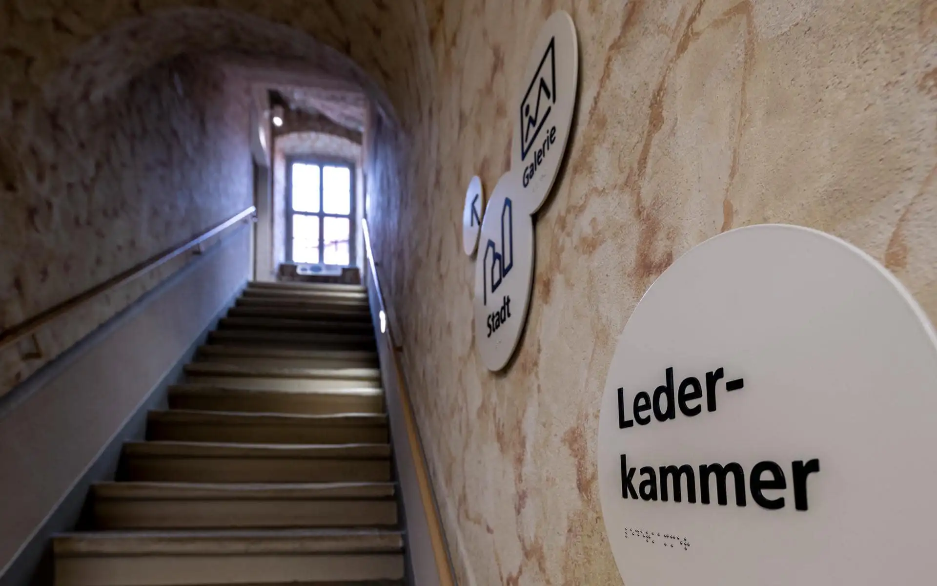 Treppenaufgang im Museum Lohgerber mit runden Leitsystem-Schildern inklusive Braille.