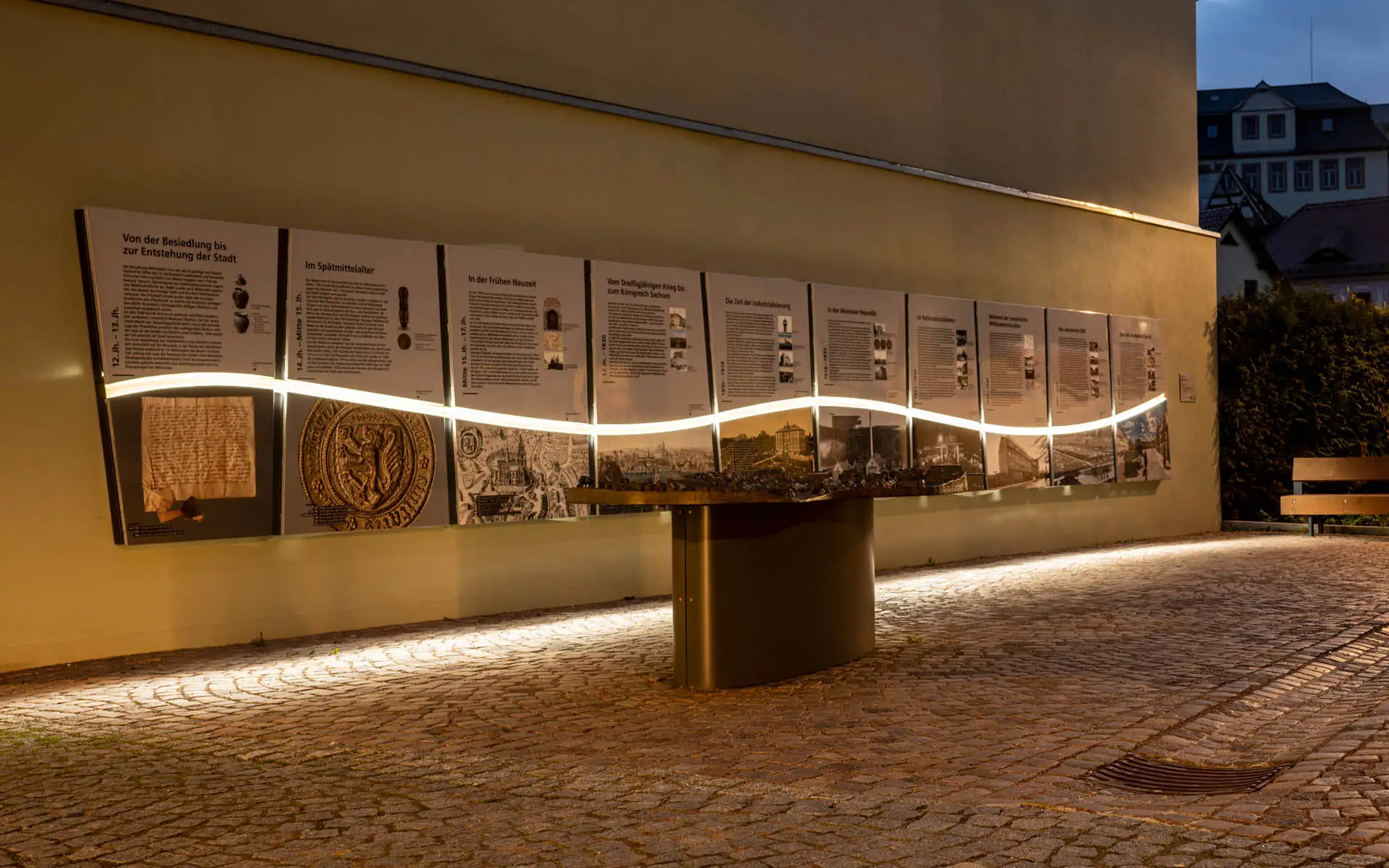 Abendausleuchtung einer historischen Wandinstallation mit Infotafeln und Stadtmodell in Mittweida.