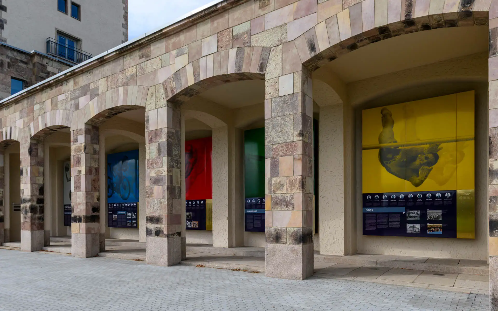 Detailansicht der Arkaden des Sportforums mit farbigen Grafiken und Infotafeln.