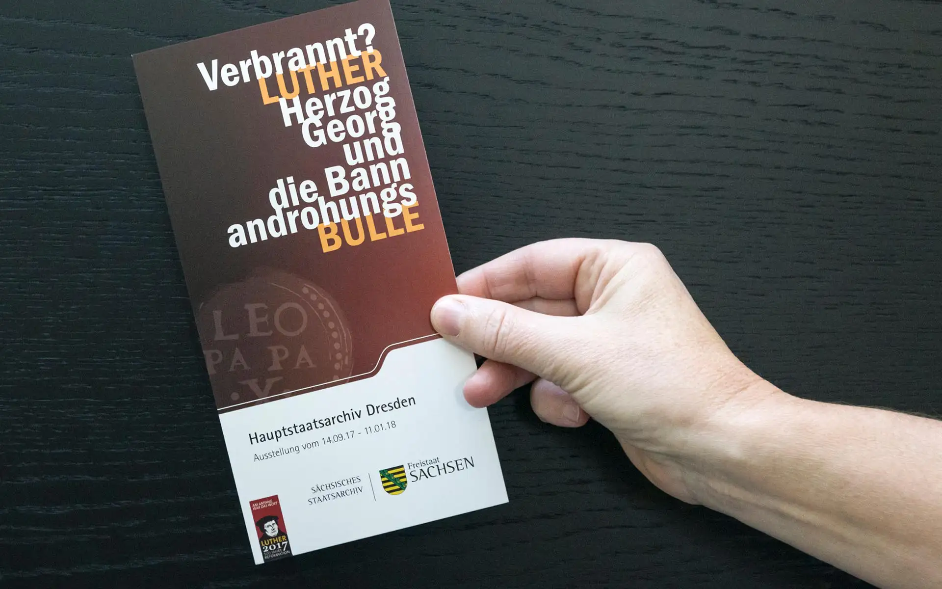 Ausstellungsflyer zur Luther-Ausstellung im Hauptstaatsarchiv Dresden, gehalten in dunklen Brauntönen mit typografischem Schwerpunkt.