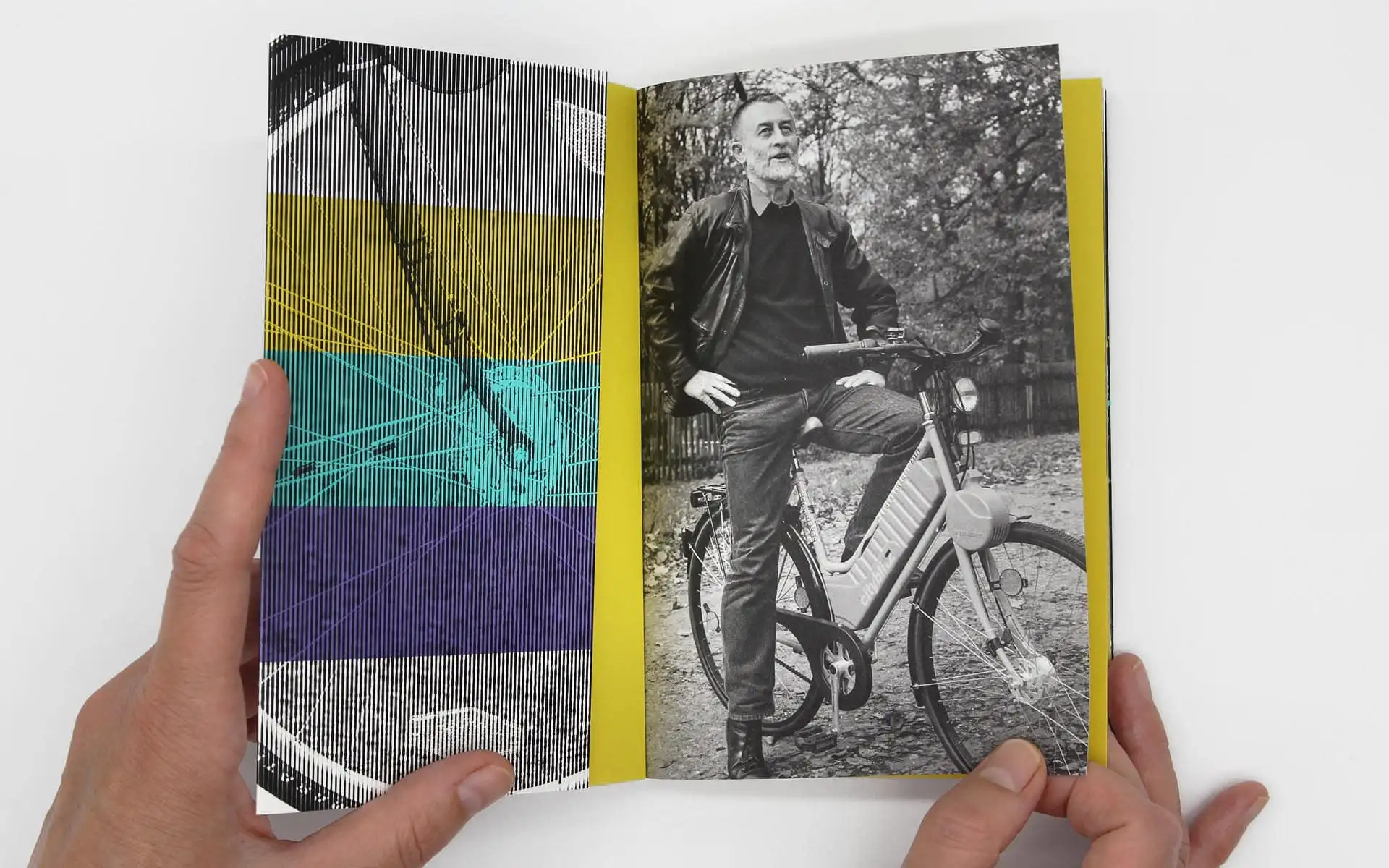 Aufgeschlagenes Buch: links grafisches Muster in Farbbändern, rechts Schwarzweißfoto einer Person auf einem Fahrrad.