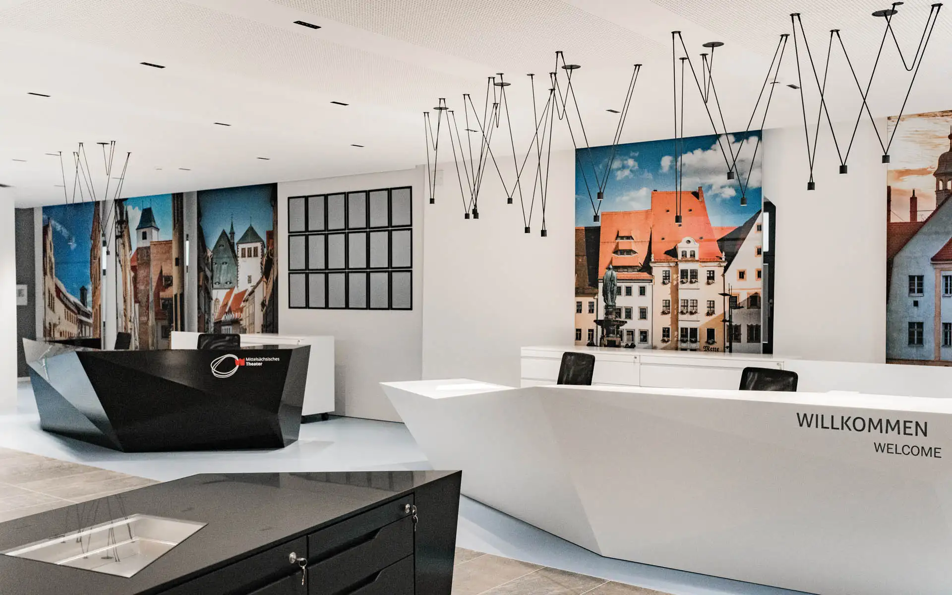 Empfangsbereich einer Tourist-Information mit weißem und schwarzem Tresen vor großformatigen Stadtmotiven