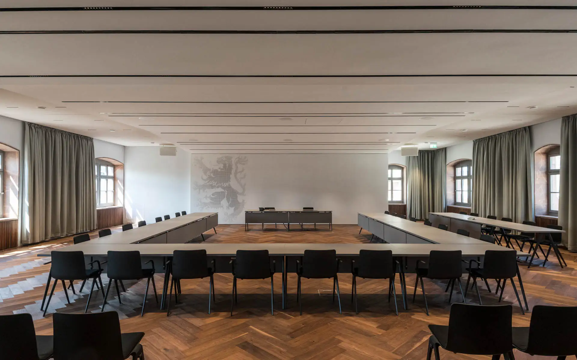 Tagungssaal mit U-förmiger Tischanlage, Parkett und Wandgrafik eines Löwen
