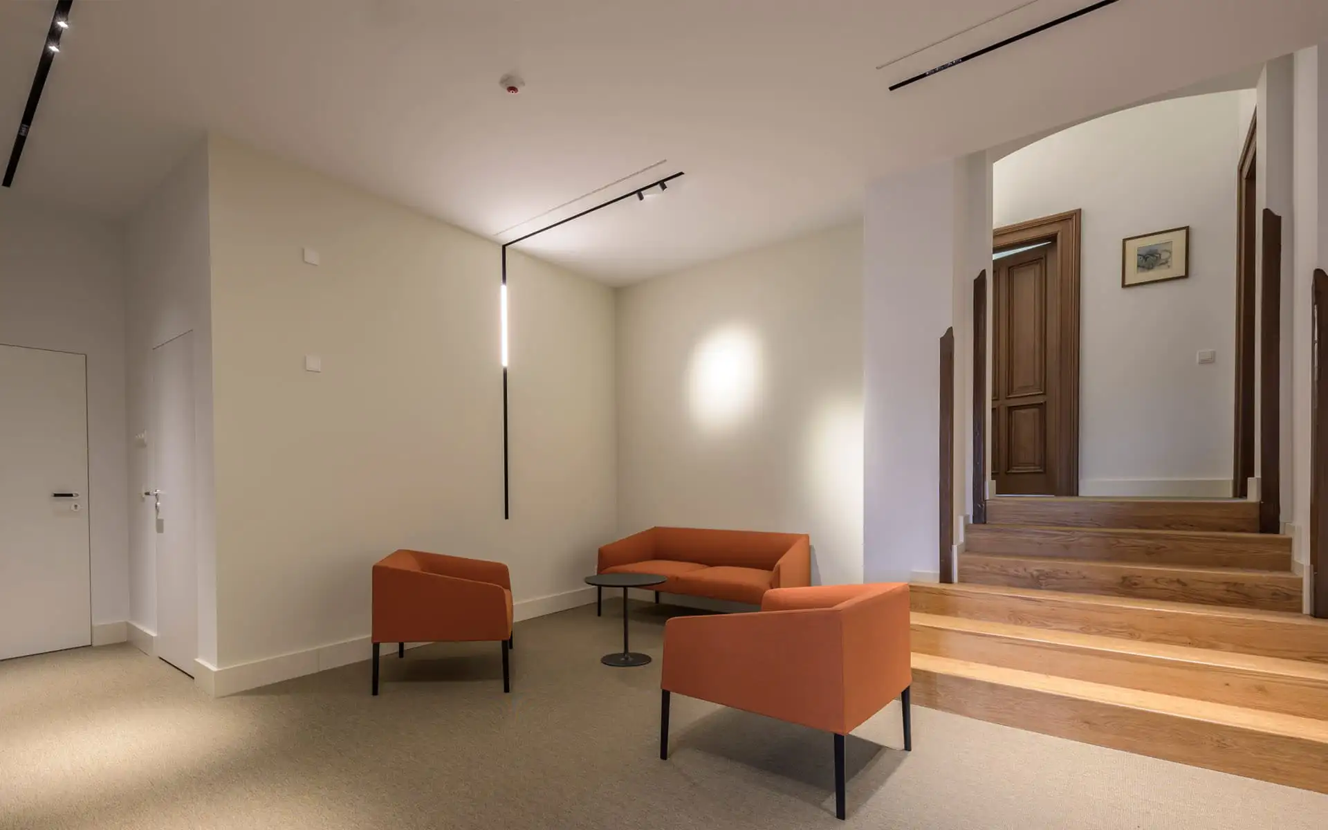 Sitzbereich mit orangefarbenen Sesseln und Sofa neben einer Treppe