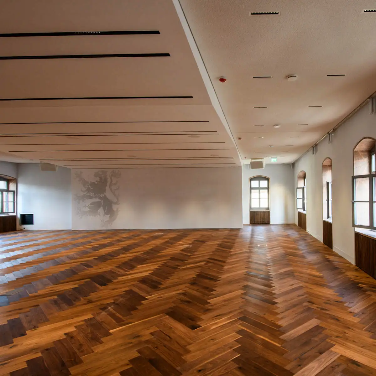 Leer geräumter Saal mit großem Fischgrätboden und Löwengrafik an der Stirnwand