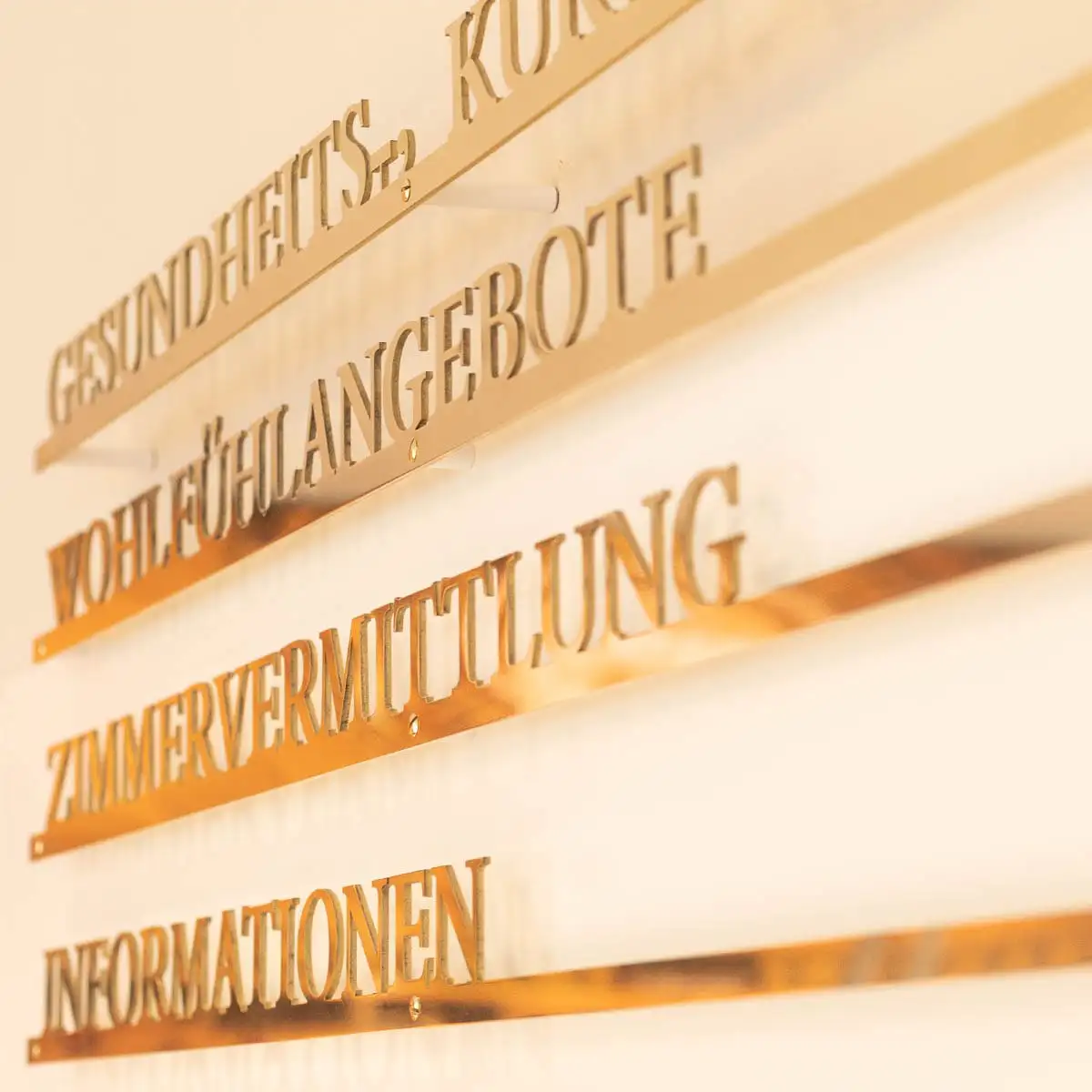 Goldfarbene Wandbeschriftung mit Kategorien wie „Wohlfühlangebote“, „Zimmervermittlung“ und „Informationen“.