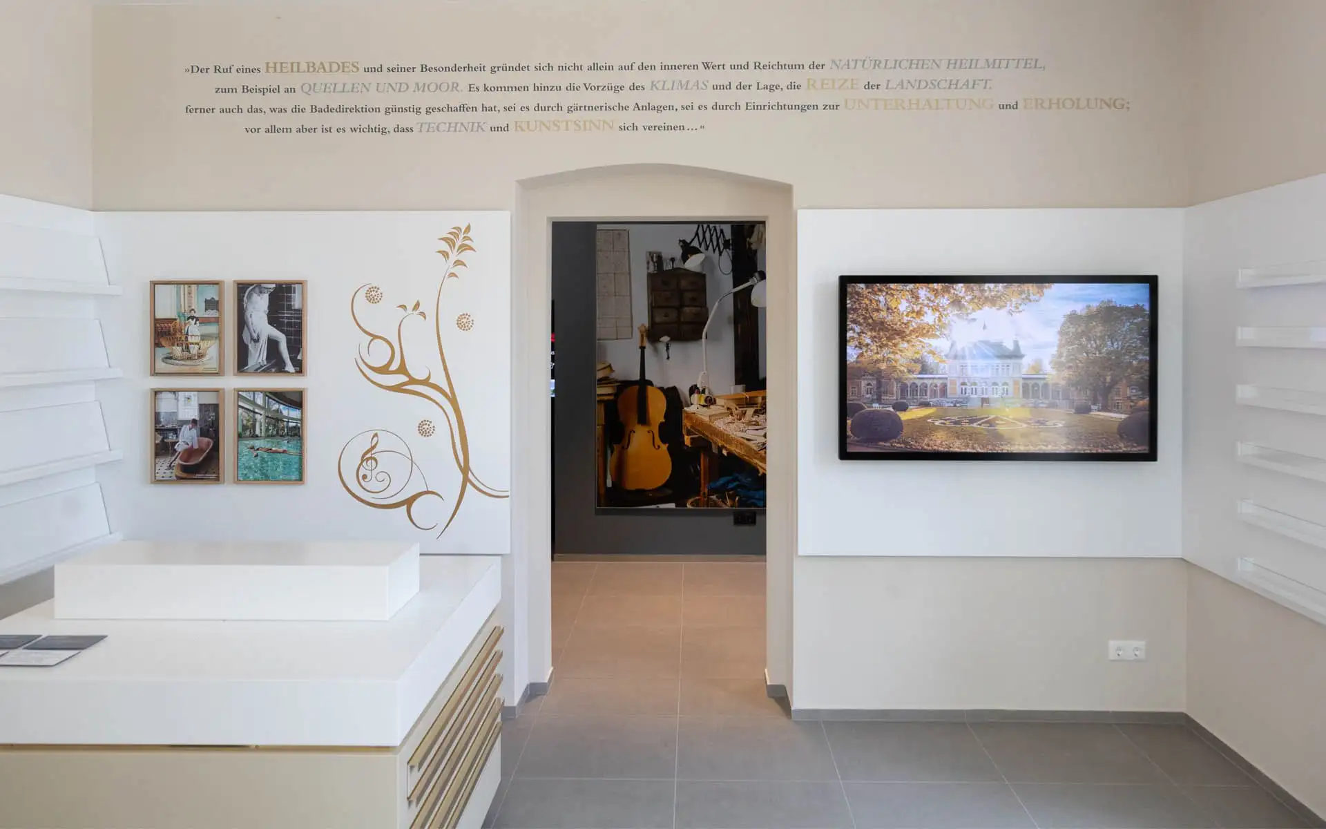 Weißes Mobiliar, goldener Wandgrafik und Bildschirm; Durchgang zu einer Fotowand.