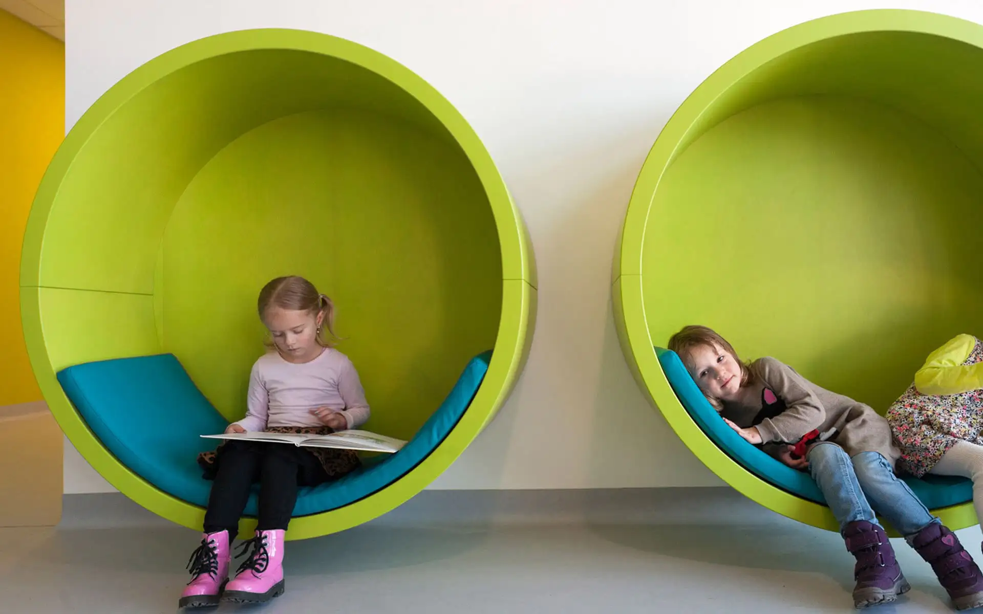 Zwei runde Sitznischen mit grünen Innenflächen, darin lesende und ruhende Kinder