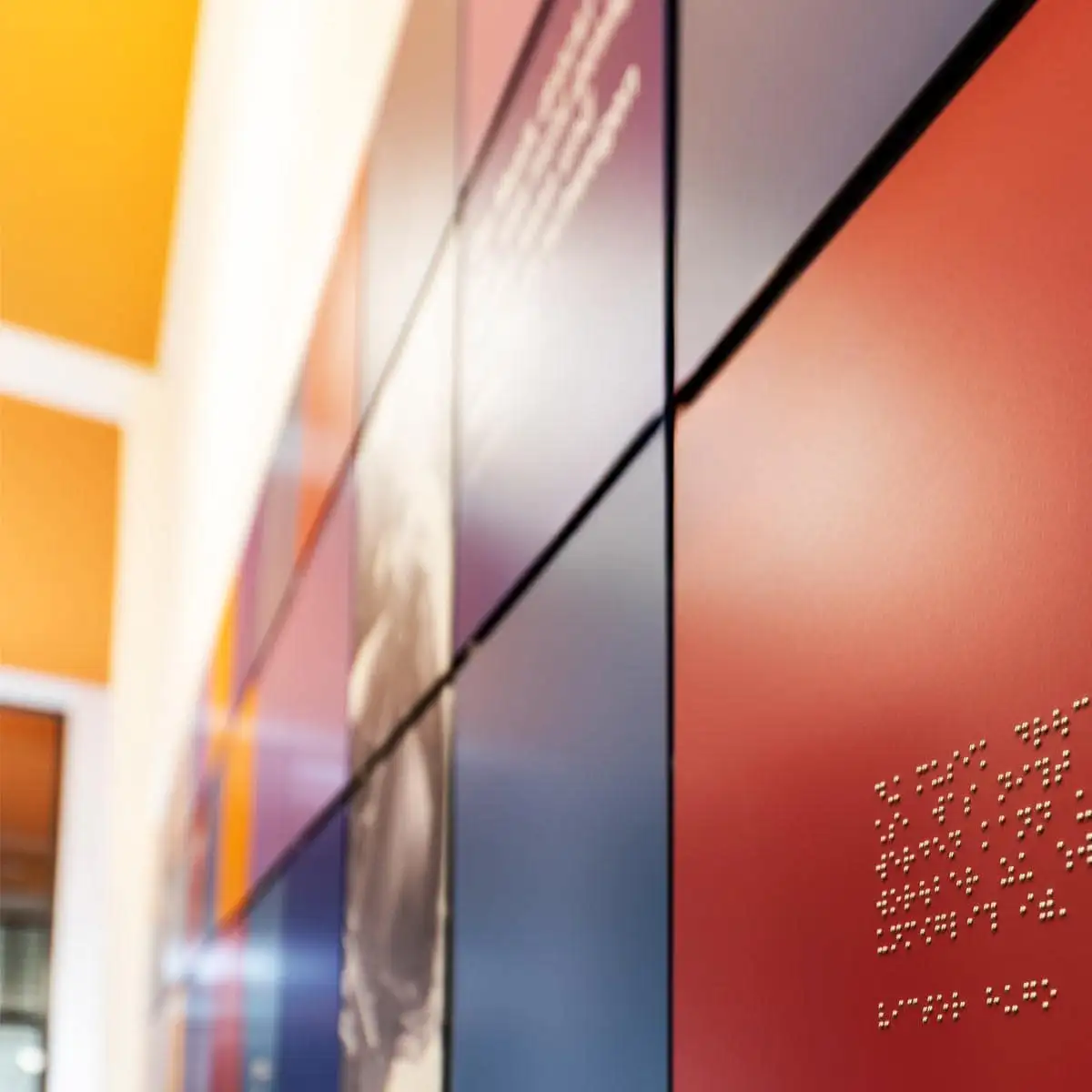 Nahaufnahme der farbigen Paneele mit Brailleschrift in erhabenen Punkten.