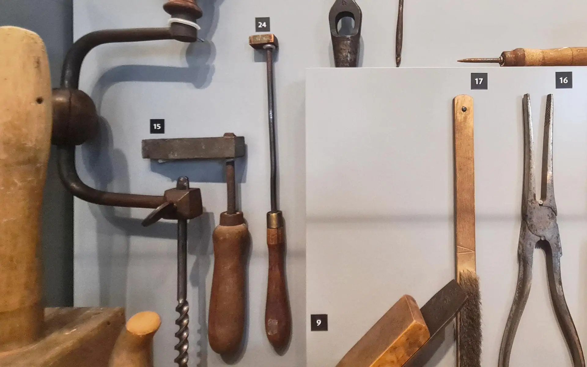 Sammlung historischer Werkzeuge mit Holzgriffen und Metallteilen, wandmontiert und nummeriert.