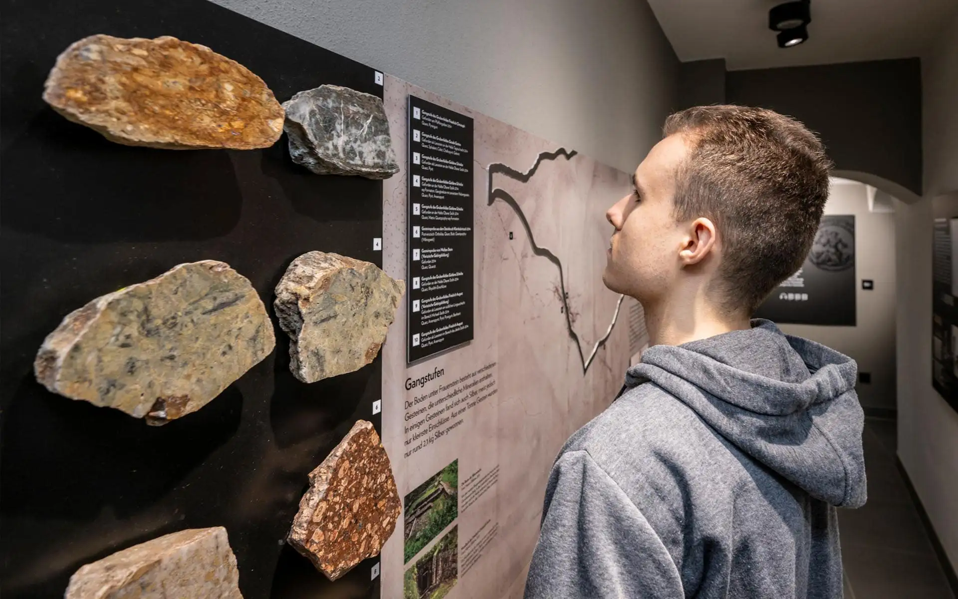 Besucher betrachtet eine geologische Ausstellung mit verschiedenen Gesteinsproben und erklärenden Texttafeln.