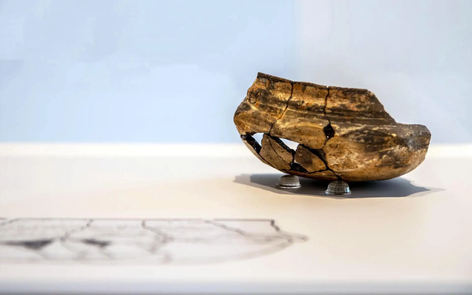 Archäologisches Fundstück auf kleiner Halterung vor neutralem Hintergrund.