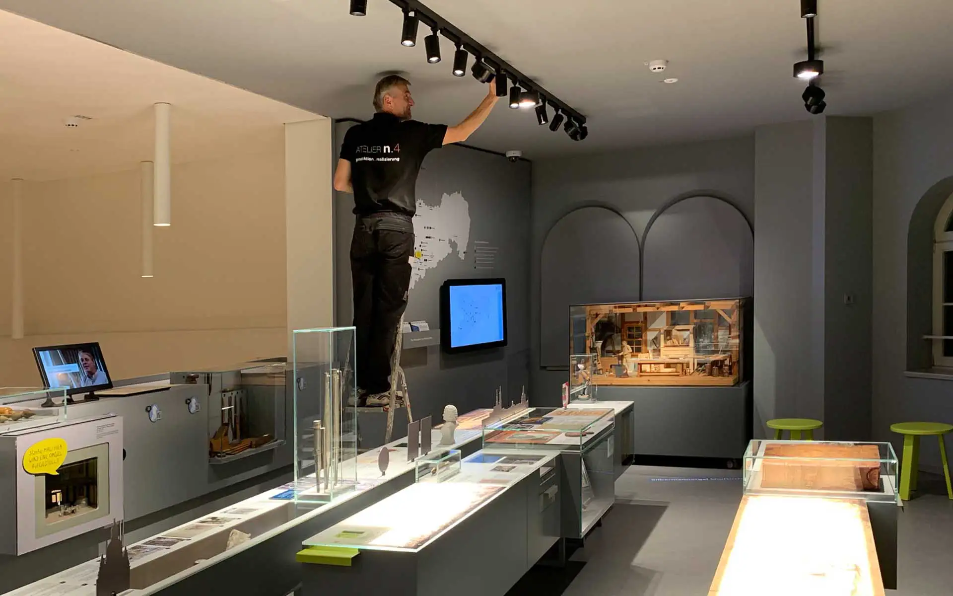 Mitarbeiter von ATELIER n.4 justiert Deckenspots zur präzisen Ausleuchtung von Exponaten in einer Museumsausstellung.