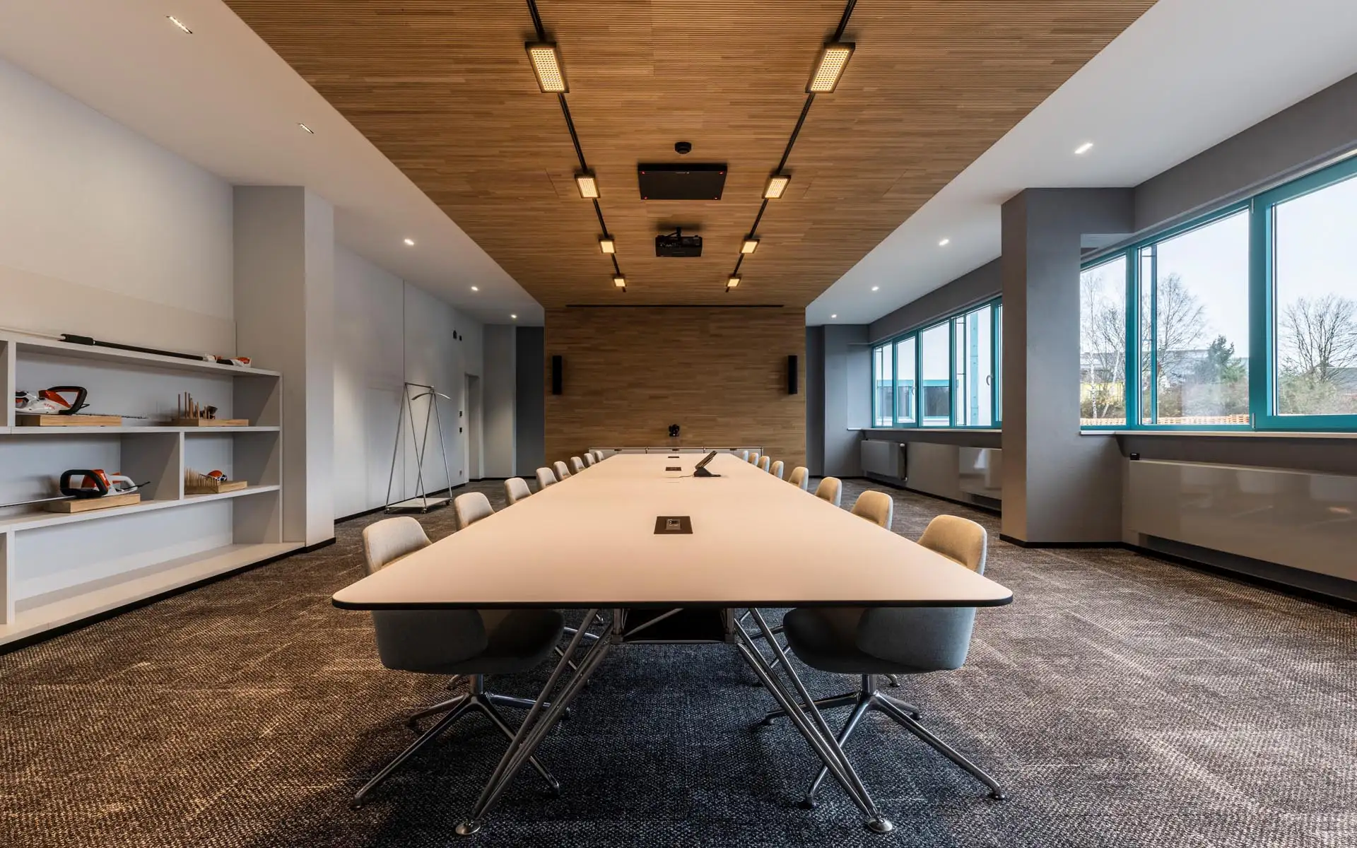 Moderner Konferenzraum mit langem Besprechungstisch, Holzdecke, integrierter Beleuchtung und großen Fensterflächen.