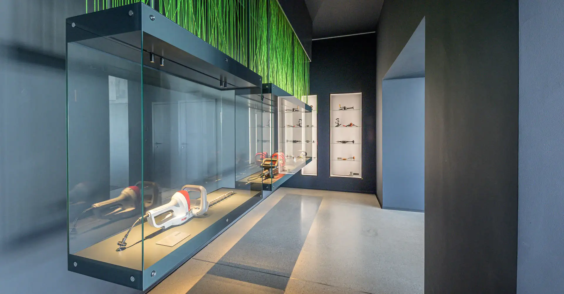 Schmaler Raum mit großer Glasvitrine links und beleuchteten Wandnischen hinten; darin liegen mehrere technische Exponate.