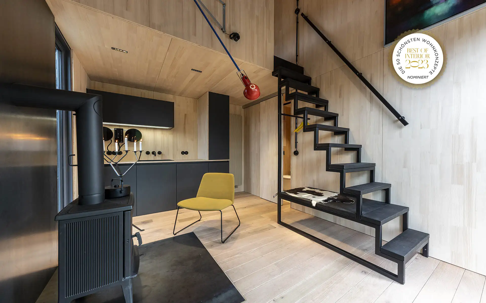 Innenraum mit Kaminofen, gelbem Stuhl und offener Metalltreppe – Best of Interior 2023 nominiert