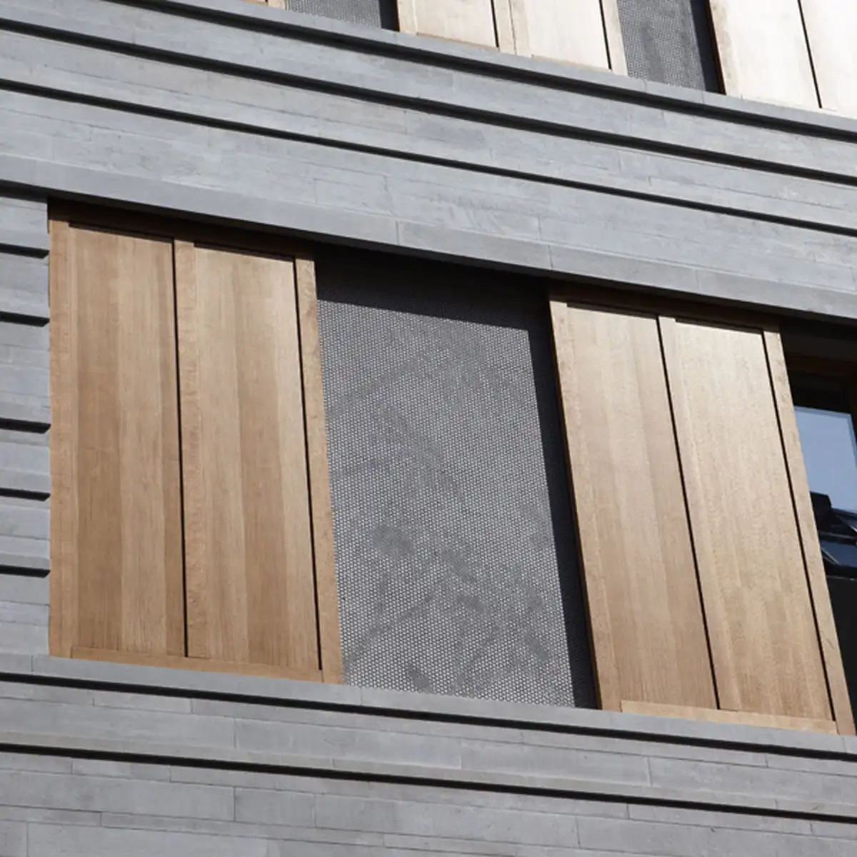 Fassadendetail: horizontale Betonbänder mit integrierten Holzschiebeläden und perforiertem Metallfeld.